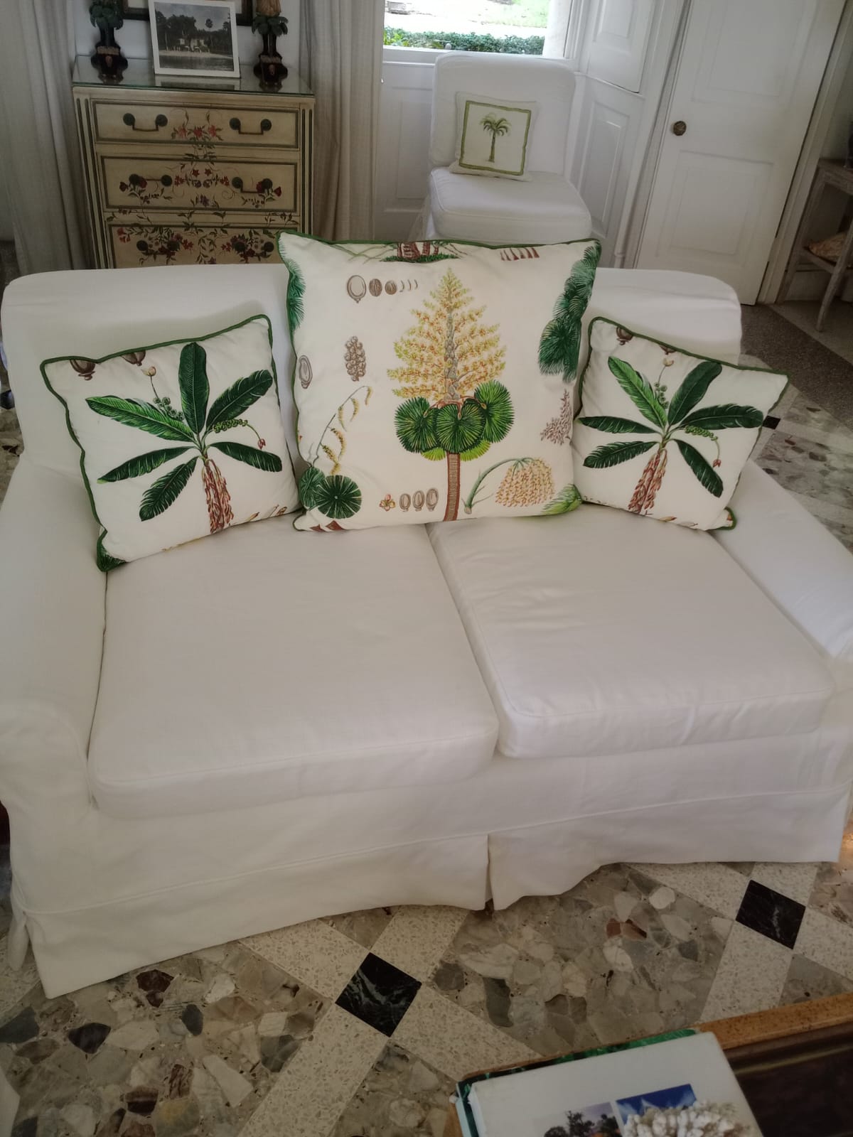 White slipcovered loveseat with palm-print piped cushions upholstered in Barbados
